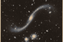 Uma lente gravitacional cósmica, formada pelo aglomerado de galáxias MACS J0138.0-2155, amplifica e distorce a luz da distante galáxia MRG-M0138, revelando segredos de um buraco negro supermassivo adormecido.